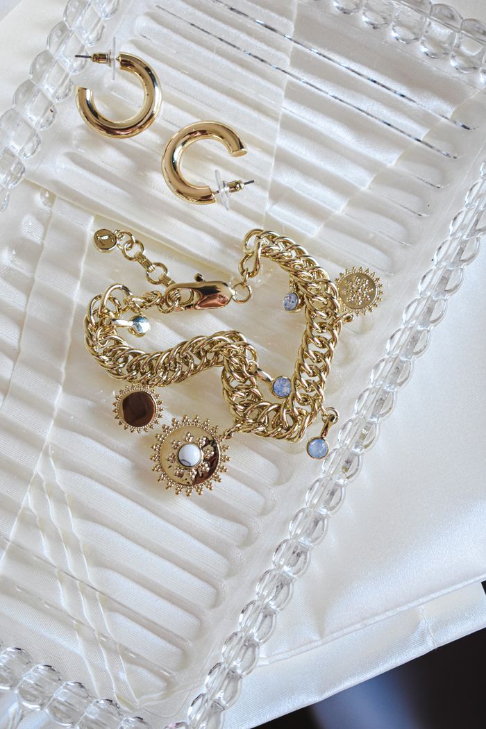 Close-up of gold jewelry with earrings and bracelet on a decorative glass tray.