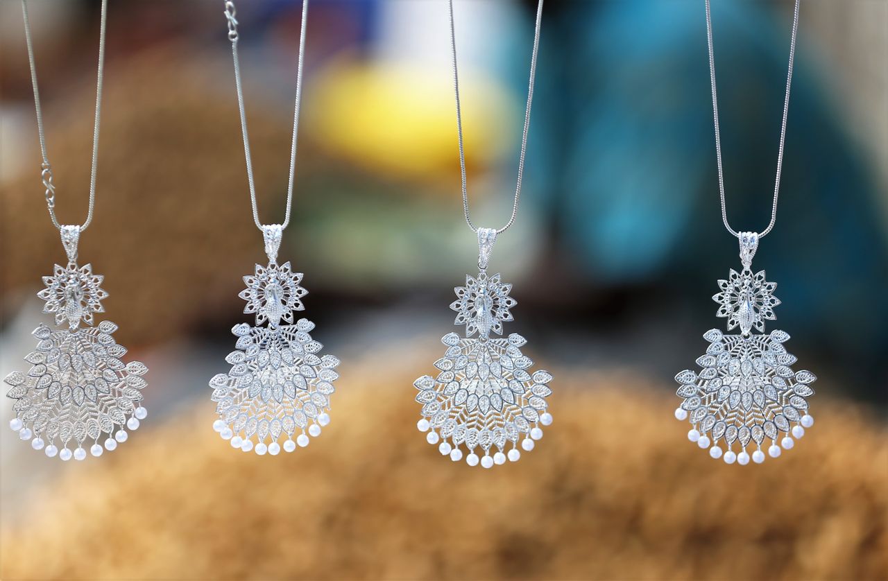 Services Close-up of beautiful silver necklaces with intricate designs hanging with a blurred background.