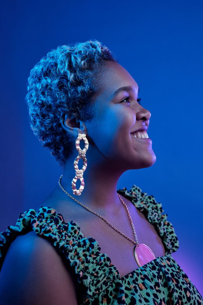 Services A vibrant profile portrait of a smiling woman adorned with fashionable earrings and necklace against a colorful backdrop.