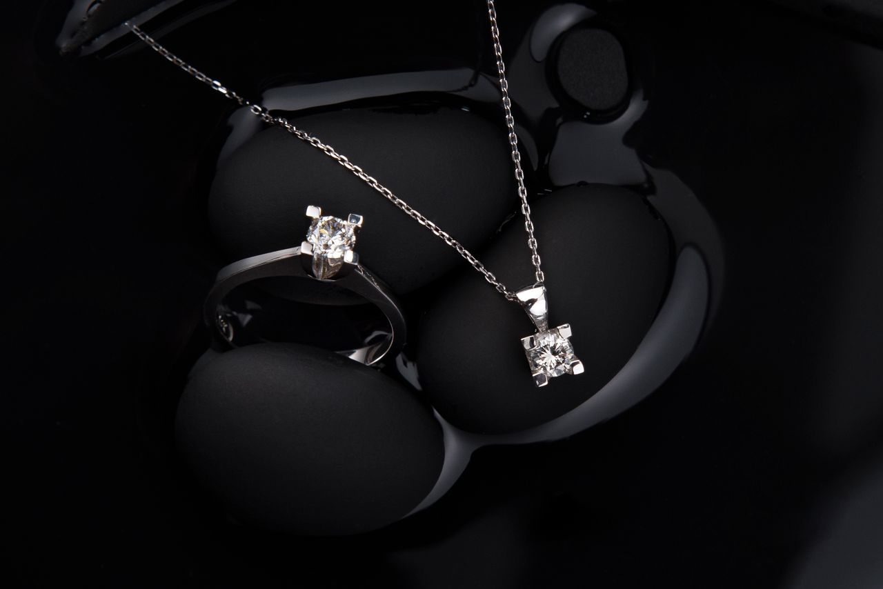 Services Luxurious silver diamond ring and pendant necklace on a black background, showcasing elegance and sophistication.