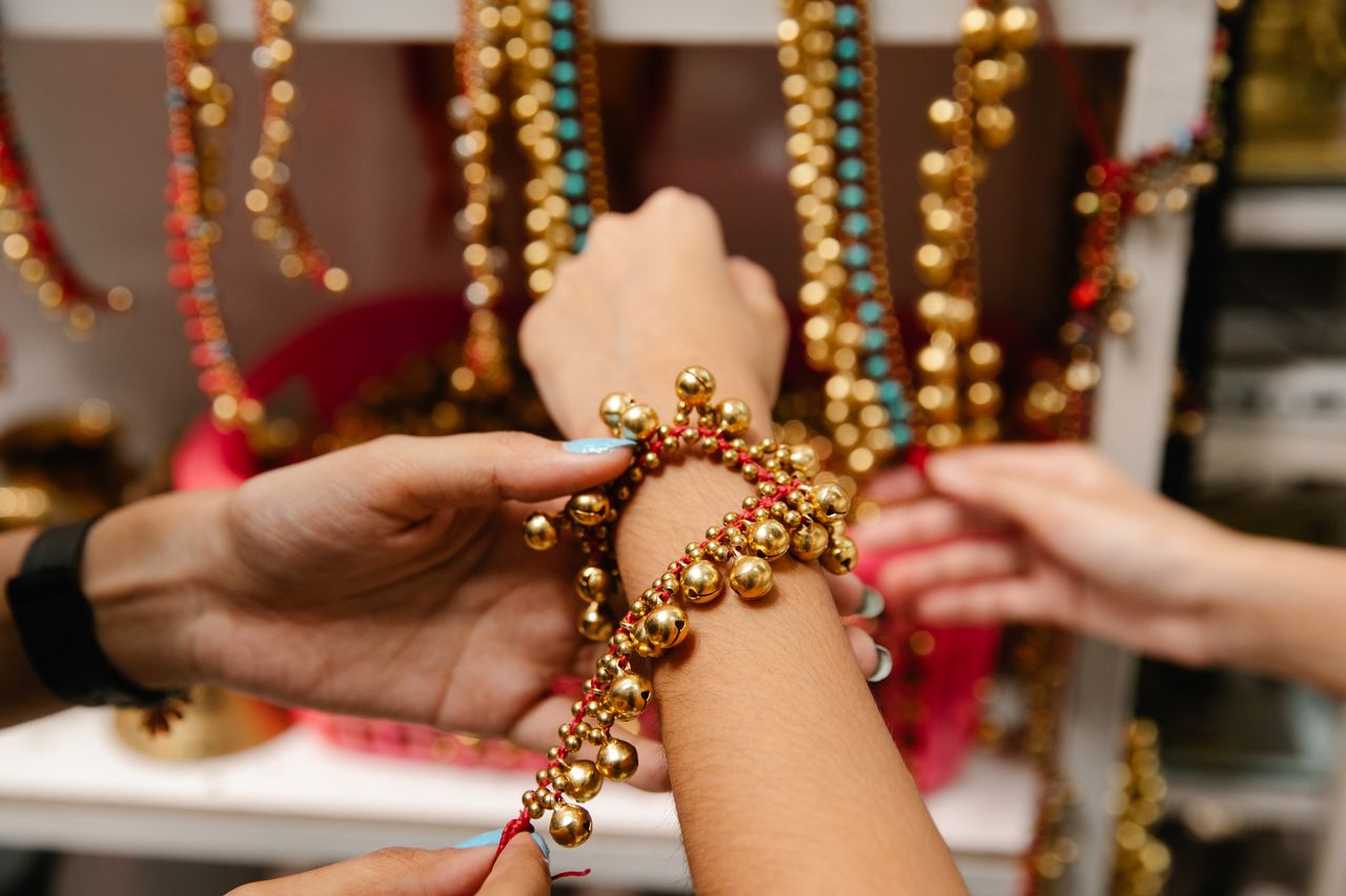 About Hands arrange a vibrant gold and red beaded bracelet with colorful beads in the background.